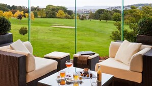 Eine Terrasse mit Korbmöbeln, einem Tisch mit Getränken und Blick auf einen Golfplatz.