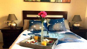 A neatly made bed with a tray of breakfast, a vase with flowers, and two lamps on nightstands.