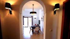 A hallway leading to a dining area with a table and chairs, a ceiling light, and wall-mounted lamps.