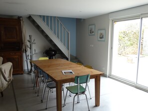 A dining area with a wooden table and chairs, a staircase, and a view through a large window.