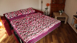 A room with a bed, a small wooden table, a cabinet, and a vase with flowers.