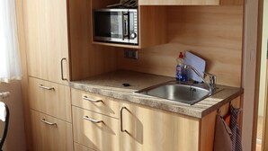 A compact kitchen with wooden cabinets, a built-in microwave, a sink, and a countertop.