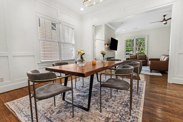 A dining area with a wooden table, six chairs, a rug, and a TV mounted on the wall.