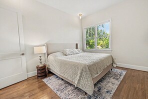 A bedroom with a bed, a window with blinds, a lamp, and a rug.