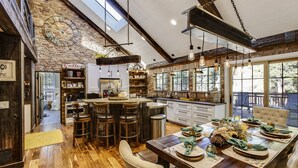 A spacious kitchen with a rustic brick wall, wooden bar stools, and a large dining table set for a meal. - Ranked #1 by VRBO in Flagstaff for 4 years! AC, Pets and Hot Tub! (Flagstaff)
