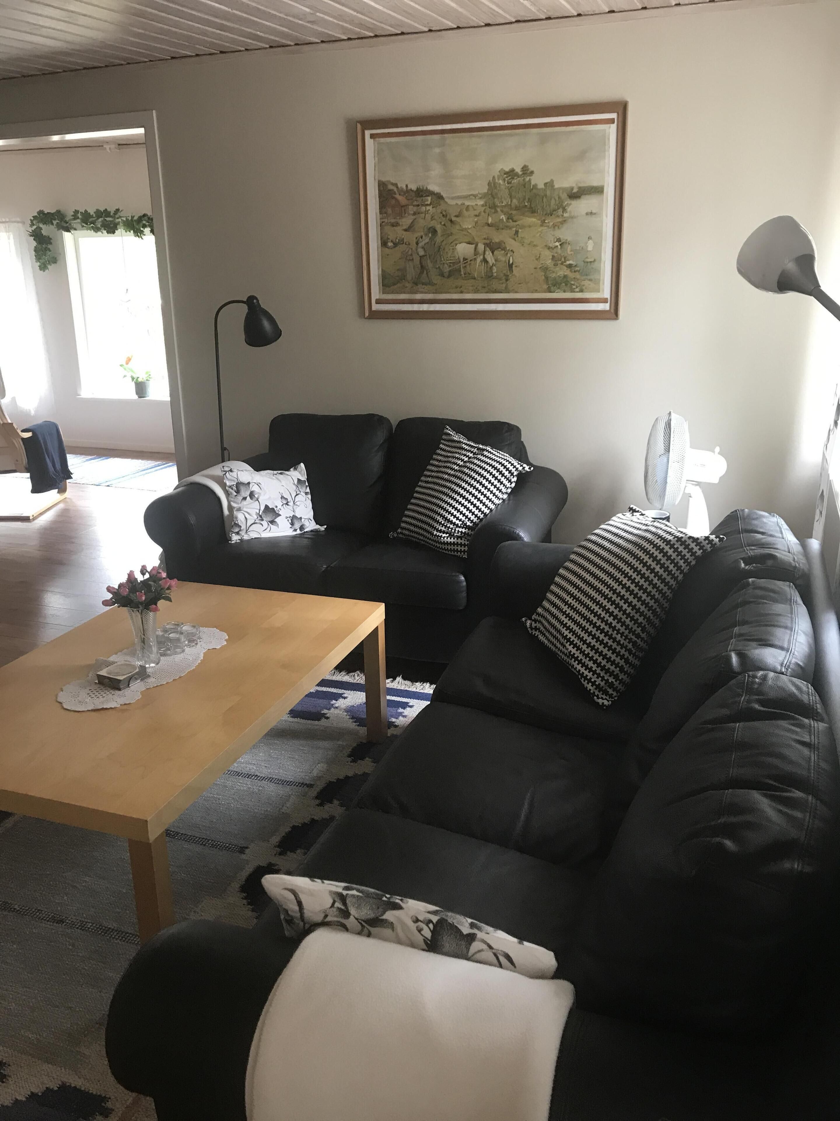 Ein Wohnzimmer mit einem schwarzen Ledersofa, einem Holztisch und einem Bild an der Wand.