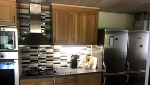 A modern kitchen with wooden cabinets, stainless steel appliances, and a tiled backsplash. - Seglarvägen 18 - House in south-east Sweden - Oknö, Mönsterås (Oknö)