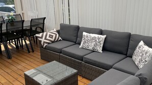 A covered outdoor seating area with a sofa, ottoman, and dining table. - Seglarvägen 18 - House in south-east Sweden - Oknö, Mönsterås (Oknö)