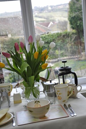 A table set with a floral bowl, a coffee pot, and a vase with tulips.