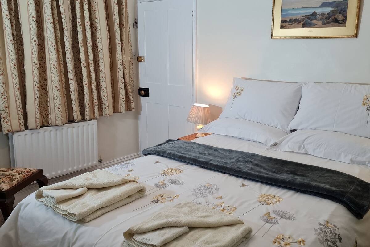 A neatly made bed with floral bedding, a bedside lamp, and a framed picture on the wall.