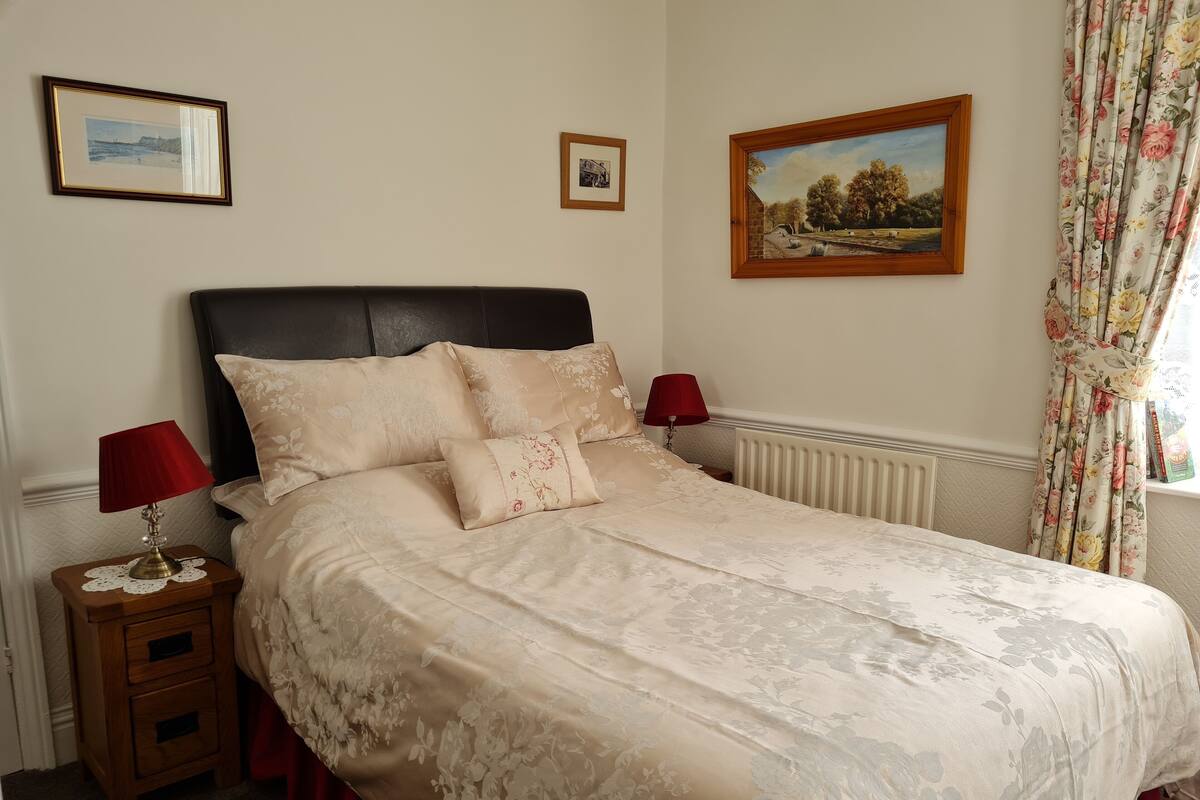 A bedroom with a large bed, two bedside tables, a nightstand, and a window with curtains.