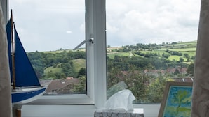 Ein Fenster mit Blick auf eine grüne Landschaft, ein Modell eines Segelbootes und ein gerahmtes Bild.