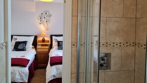Ein Hotelzimmer mit zwei Betten, einem Nachttisch mit Lampe, einem Wandbild und einem Duschbereich mit Glastür.