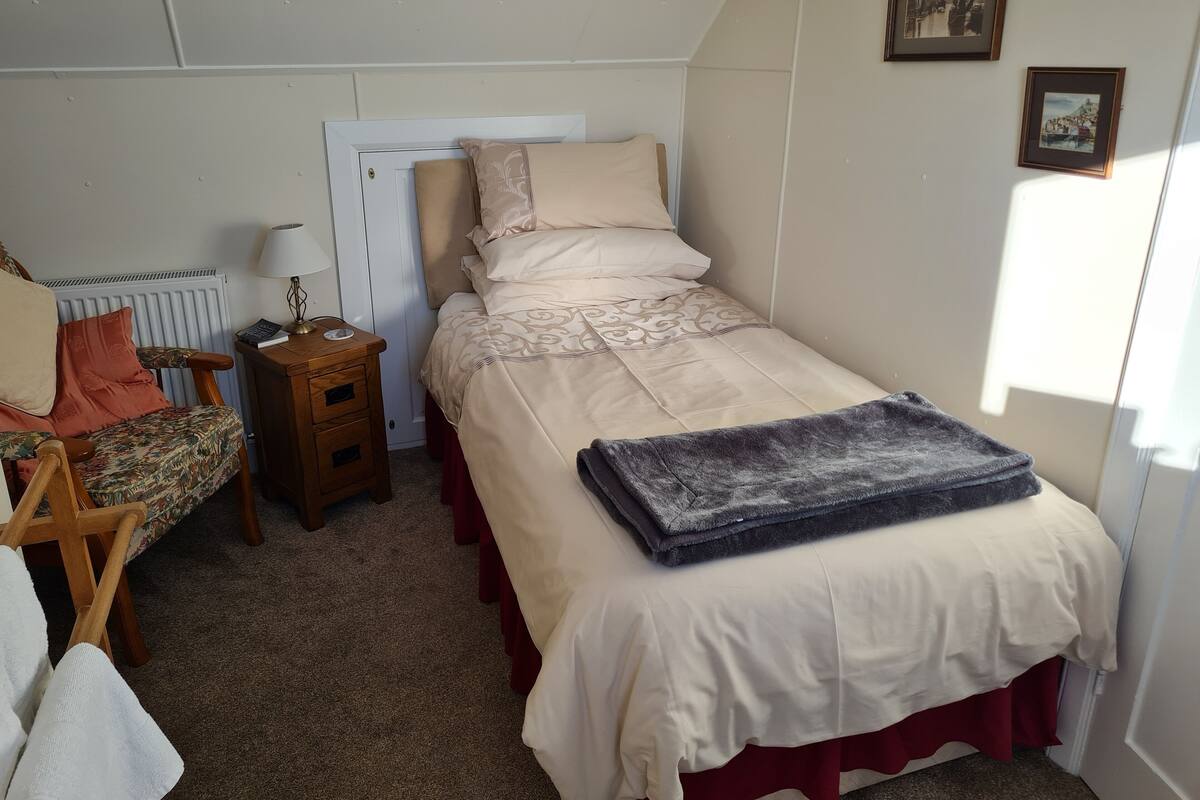 A small, neatly arranged bedroom with a single bed, a nightstand, a chair, and a radiator.