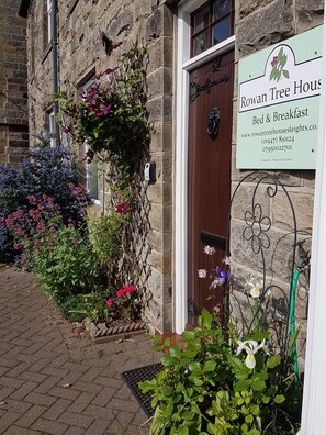 A stone building with a sign for Rowan Tree House Bed & Breakfast, featuring a wooden door and a flower garden in front. - Rowan Tree House B&B (Whitby)