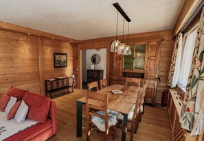 Um interior em madeira com mesa de jantar, cadeiras, sofá e cozinha.
