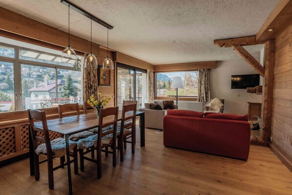 Interior de madeira com uma mesa de jantar, cadeiras, um sofá vermelho e uma TV na parede.