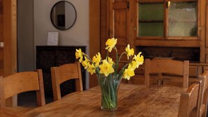 A wooden dining table with chairs, a vase of yellow flowers, and hanging pendant lights.