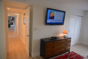 Habitación de hotel con una televisión mostrando un programa de eventos, un aparador de madera y una alfombra roja.