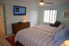 A bedroom with a bed, a dresser, a television mounted on the wall, a window with blinds, and a ceiling fan. - Marquise 204 Beachfront 2br, 2 Bath condo-Directly on Beach! (Indian Rocks Beach)