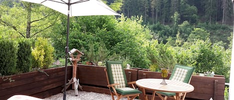 Un patio al aire libre con una mesa y sillas de madera, un comedero para pájaros y una sombrilla.