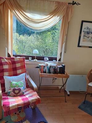 A cozy room with a view of trees through a window, a wicker table with books and a lamp, and a checkered sofa with decorative pillows. - *** Star apartment, large terrace on the south slope with panoramic views near the Rursee (Simmerath)
