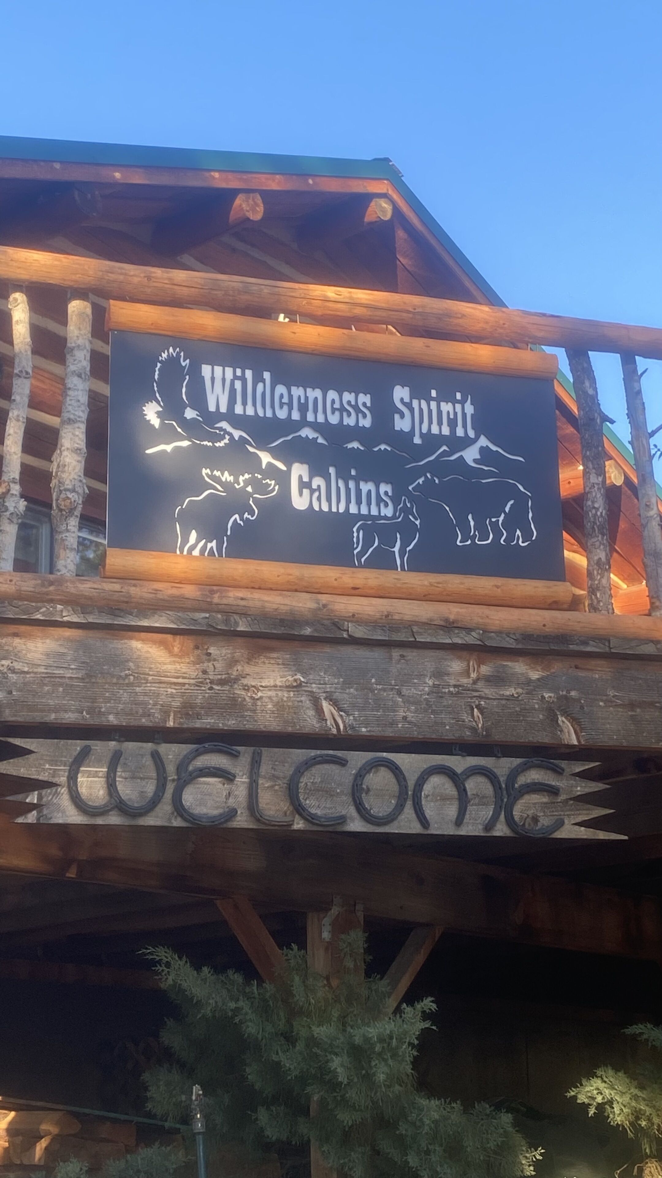 A wooden cabin with a sign that reads "Wilderness Spirit Cabins" and a "Welcome" sign below.
