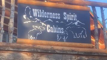 A wooden cabin with a sign that reads "Wilderness Spirit Cabins" and a "Welcome" sign below.