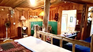 A rustic room with a bed, a chair, a table, and a mirror. - Wilderness Spirit Cabins 'Bear Cave' cabin-family friendly/sportsman paradise (Corvallis)