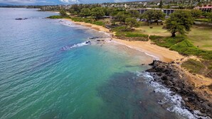 A coastal area with a sandy beach, clear turquoise waters, and a backdrop of residential buildings. - SPECIAL SUMMER BREAK RATES! Stunning Ocean View 2BR/2BA condo across KAM3 Beach! (Kihei)