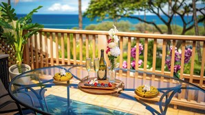 A glass-top table with a bottle, glasses, and a fruit platter on a balcony with a view of the ocean. - SPECIAL SUMMER BREAK RATES! Stunning Ocean View 2BR/2BA condo across KAM3 Beach! (Kihei)