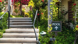 A set of outdoor stairs leading to a pool area, surrounded by lush greenery and a sign indicating the pool's direction. - SPECIAL SUMMER BREAK RATES! Stunning Ocean View 2BR/2BA condo across KAM3 Beach! (Kihei)