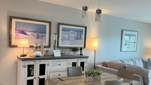A dining area with a wooden table and chairs, a white cabinet with glass doors, and two framed pictures on the wall.