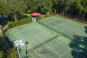 An outdoor tennis court with a red pavilion, surrounded by trees.