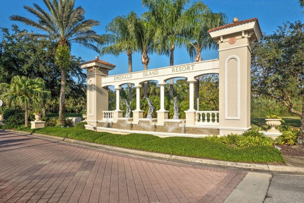 A gated entrance with 'Emerald Island Resort' signage, palm trees, and a brick pathway.