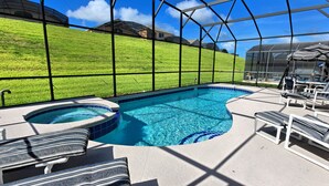 A swimming pool with a hot tub, lounge chairs, and a view of a green hillside.