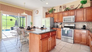 A kitchen with wooden cabinets, a large island, stainless steel appliances, and a view to a patio area.