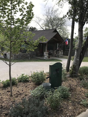 A rustic cabin with a stone foundation, a wooden roof, and a Texas flag.