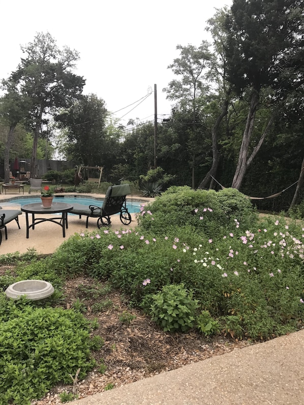 A backyard with a swimming pool, outdoor furniture, and lush greenery.