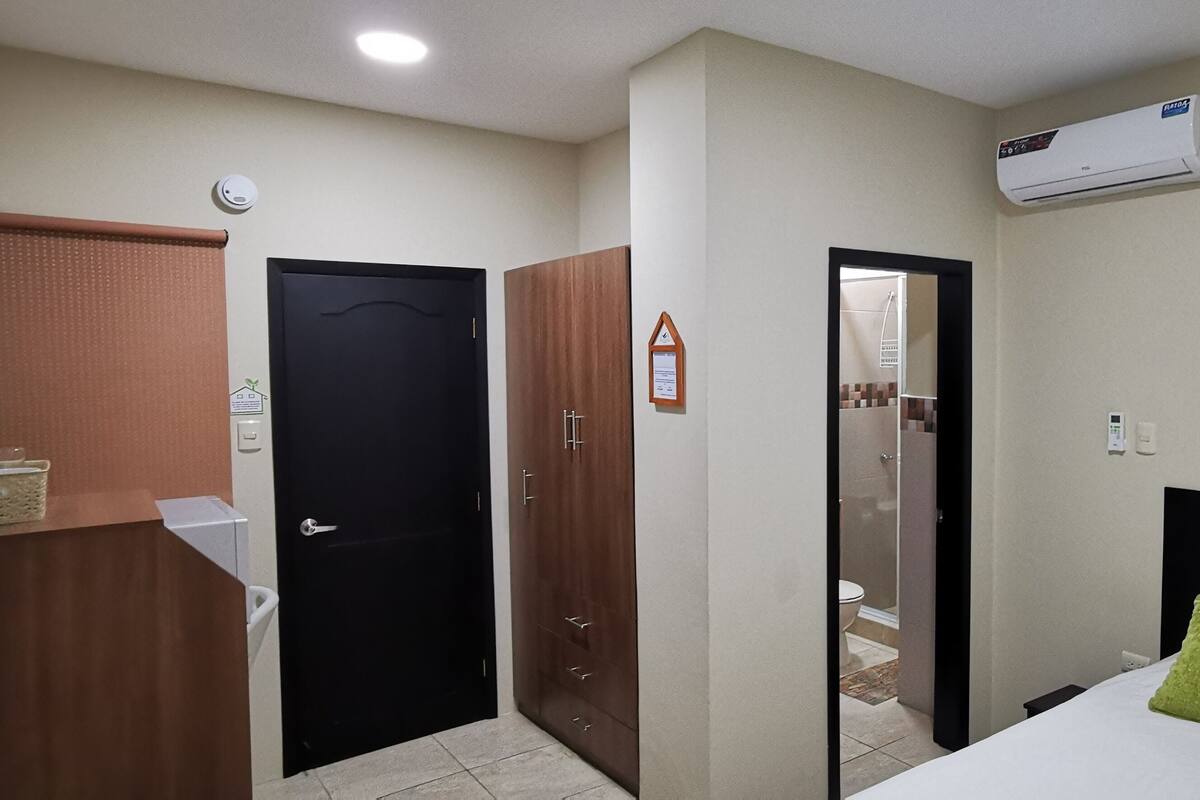 A hotel room with a bed, a desk, a wardrobe, and an air conditioning unit.