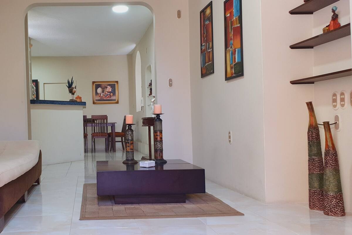 A living room with a sofa, a coffee table, and a dining area in the background.