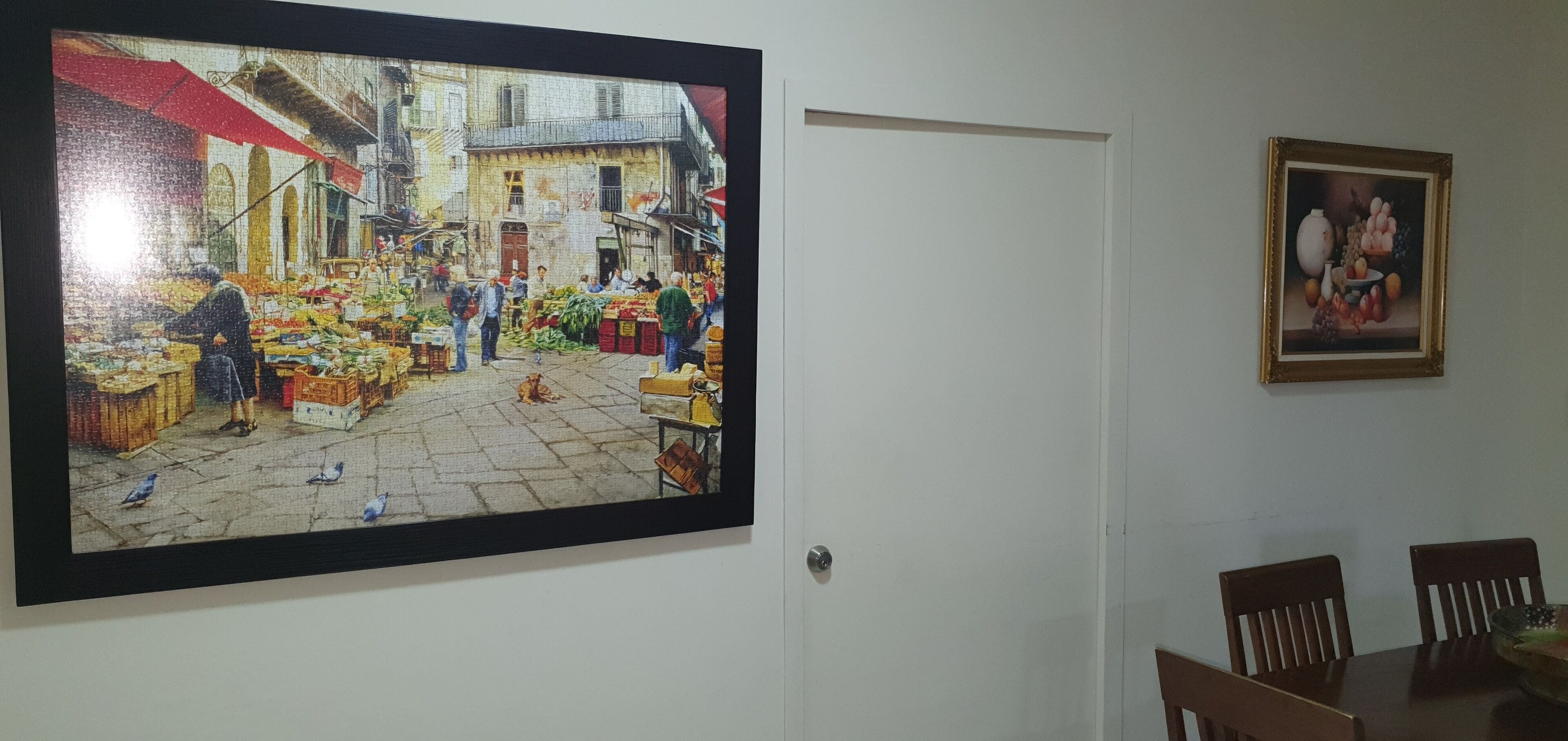 Un grand tableau encadré représentant une scène animée de marché, accroché au mur.