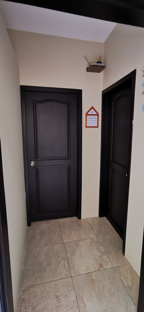 Un pasillo con dos puertas negras, paredes color beige y un estante pequeño sobre una puerta.