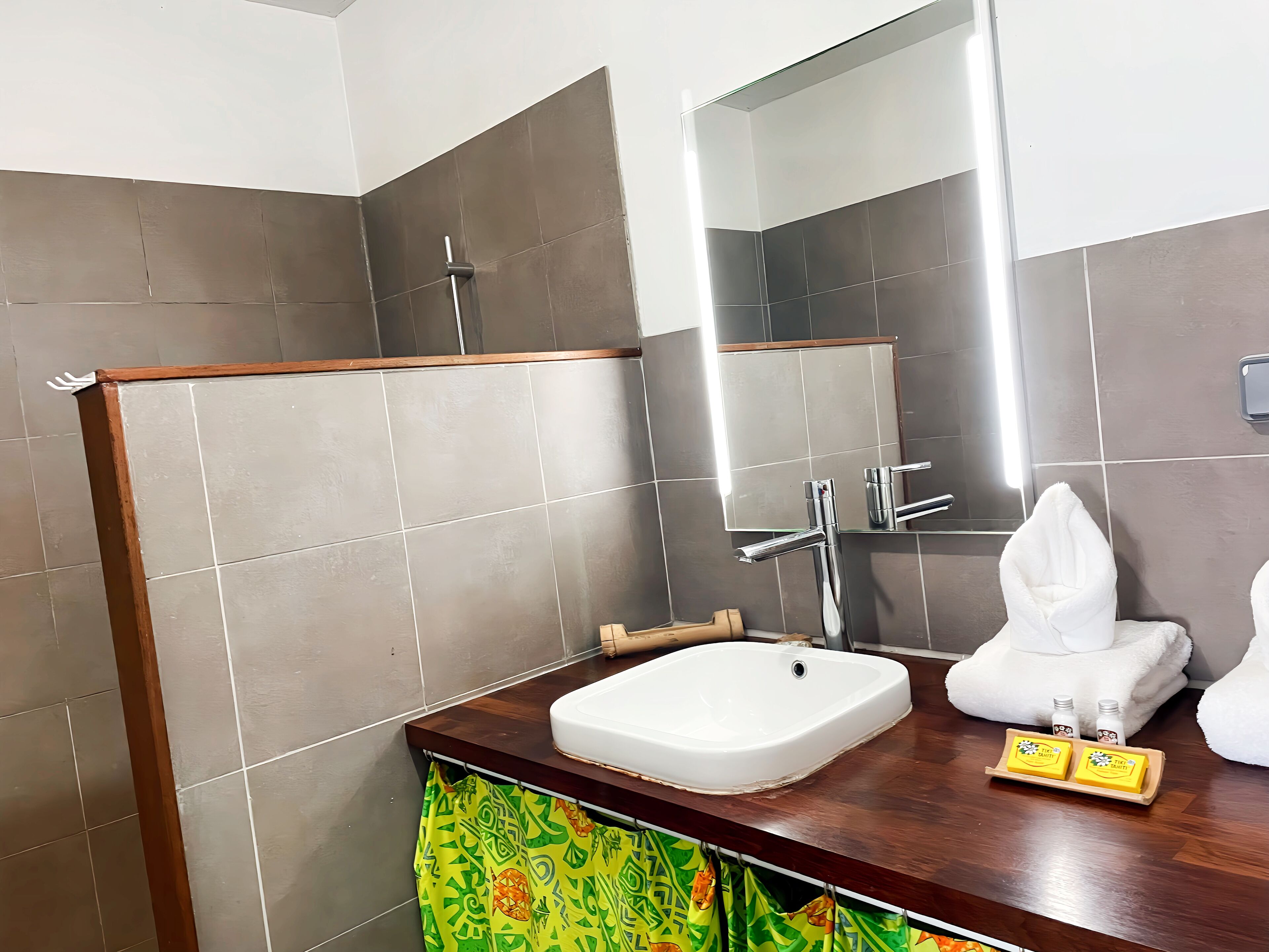 Een badkamer met een houten wastafel, een witte wasbak, een spiegel en een douchehoek.