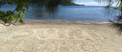 Une plage parsemée d’empreintes de pas, offrant une vue dégagée sur l’eau et les collines lointaines.