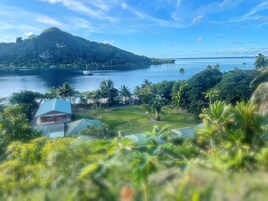 Un paisaje tropical con una masa de agua extensa, una colina y un edificio de techo azul.