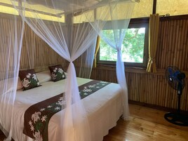 Una habitación con una cama bajo un dosel, una ventana con cortinas, un ventilador y paredes de madera.