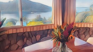 A room with a stone wall, a wooden ceiling, and a view of a mountainous landscape through two windows. - Fare Oviri Lodge (Raiatea)