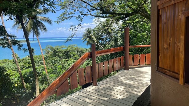 A wooden staircase leading to a balcony with a view of the ocean and tropical vegetation. - Fare Oviri Lodge (Raiatea)