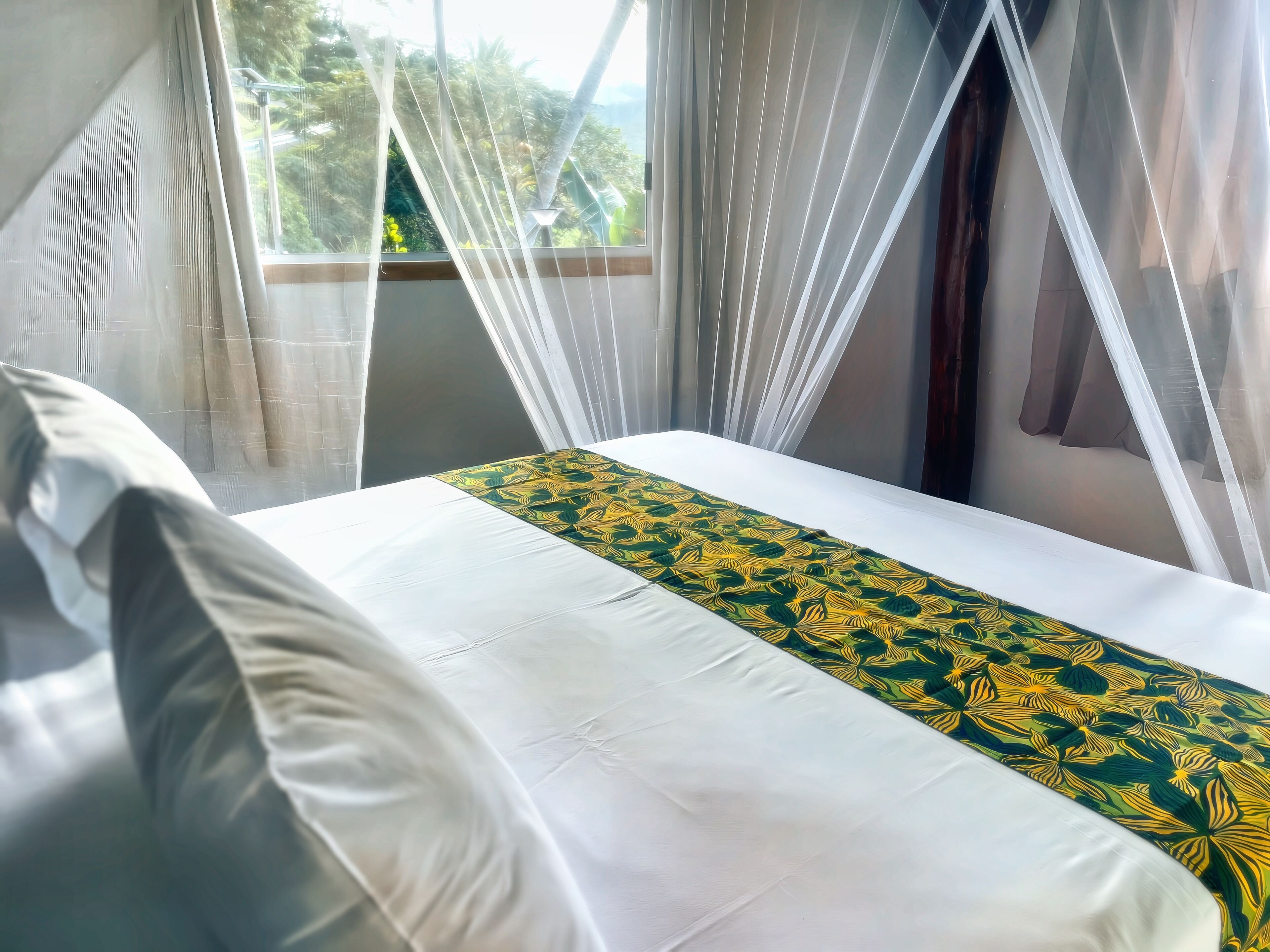 A bed with white bedding and a green and yellow patterned runner.